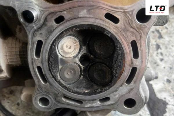 Bề mặt lòng chảo nắp xúp-páp bám đầy muội than đen kịt, cặn bẩn dầu nhớt cháy dính chặt.